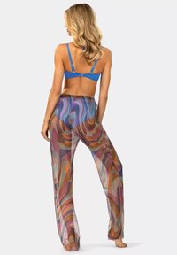 Przezroczyste, wielokolorowe szerokie spodnie z spiralnym wzorem, w połączeniu z jednolitą, niebieską biustonoszem. Materiał jest lekki i zwiewny.
