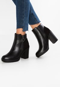 Stivaletti in pelle nera con tacco spesso, dettaglio della zip laterale e pannelli in suede a contrasto. Suola in gomma per una migliore aderenza.