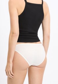 Slip bikini in cotone bianco con texture morbida e cuciture minimali, abbinati a un top nero aderente che mostra un design semplice.