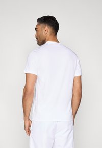 Biała bawełniana koszulka z krótkimi rękawami i okrągłym dekoltem, pokazana od tyłu, o gładkiej teksturze i swobodnym kroju.