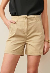 Khakifarbene Baumwollshorts mit Knopfverschluss, Vordertaschen und umgeschlagenen Säumen. Verfügen über eine glatte Textur und eine taillierte Passform.