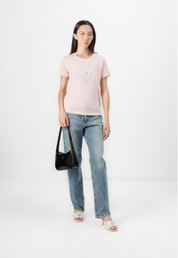 Camiseta rosa claro con un logo triangular en plata, combinada con jeans rectos azul claro, bolso negro y tacones abiertos color crema.