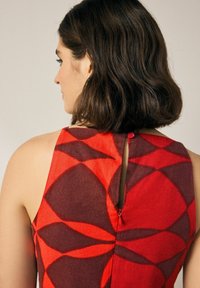 Rotes und braunes gemustertes Kleid mit einem Schlüsselaugen-Detail am Rücken und Knopfverschluss. Der Stoff wirkt weich und leicht.