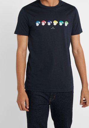Camiseta azul marino con seis caras de monos de dibujos animados de colores en fila a lo largo del pecho, combinada con jeans azul oscuro.