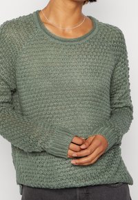 Vaaleanvihreä neulottu villapaita, jossa on teksturoitu, avoin kudontamuotoilu, ribbaatut hihansuut ja pyöreä kaula-aukko; pehmeä, rento muotoilu ja kevyt ulkonäkö.