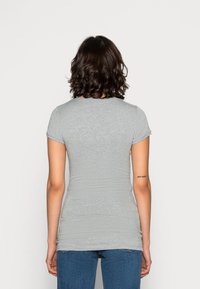 Šedé přiléhavé tričko s krátkými rukávy, kulatým výstřihem a hladkou texturou, doplněné modrými džínami z denimu. Zobrazen zadní pohled.