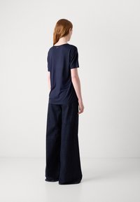 T-shirt navy a maniche corte, con girocollo e un logo discreto sulla schiena, abbinato a pantaloni in denim scuri a gamba larga.