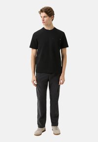 Czarna bawełniana koszulka z okrągłym dekoltem i małą kieszonką na piersi, zestawiona z ciemnoszarymi spodniami i jasnymi butami.