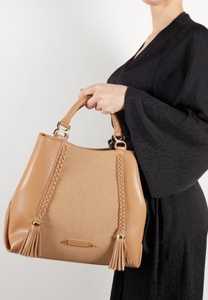 Tan håndtaske med textureret krop og flettede detaljer samt frynser, suppleret med et flettet håndtag og gul hardware.