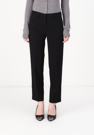 Black tailored trousers with a straight-leg fit, featuring a smooth fabric and subtle front crease. Paired with pointed black heels.