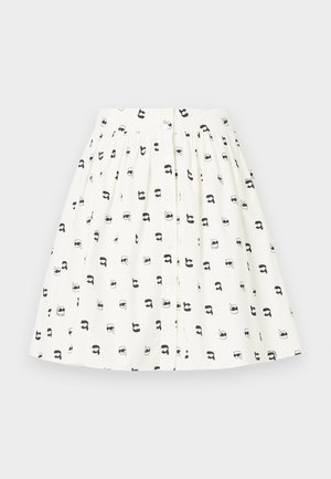 Jupe en tissu blanc avec un motif de petites têtes de dessins animés noires ornées de divers accessoires. Elle a un devant à boutons et une taille froncée.