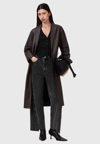 Cappotto trench in pelle marrone, top nero a costine, jeans in denim nero a vita alta e stivaletti neri a punta. Borsa nera semplice.