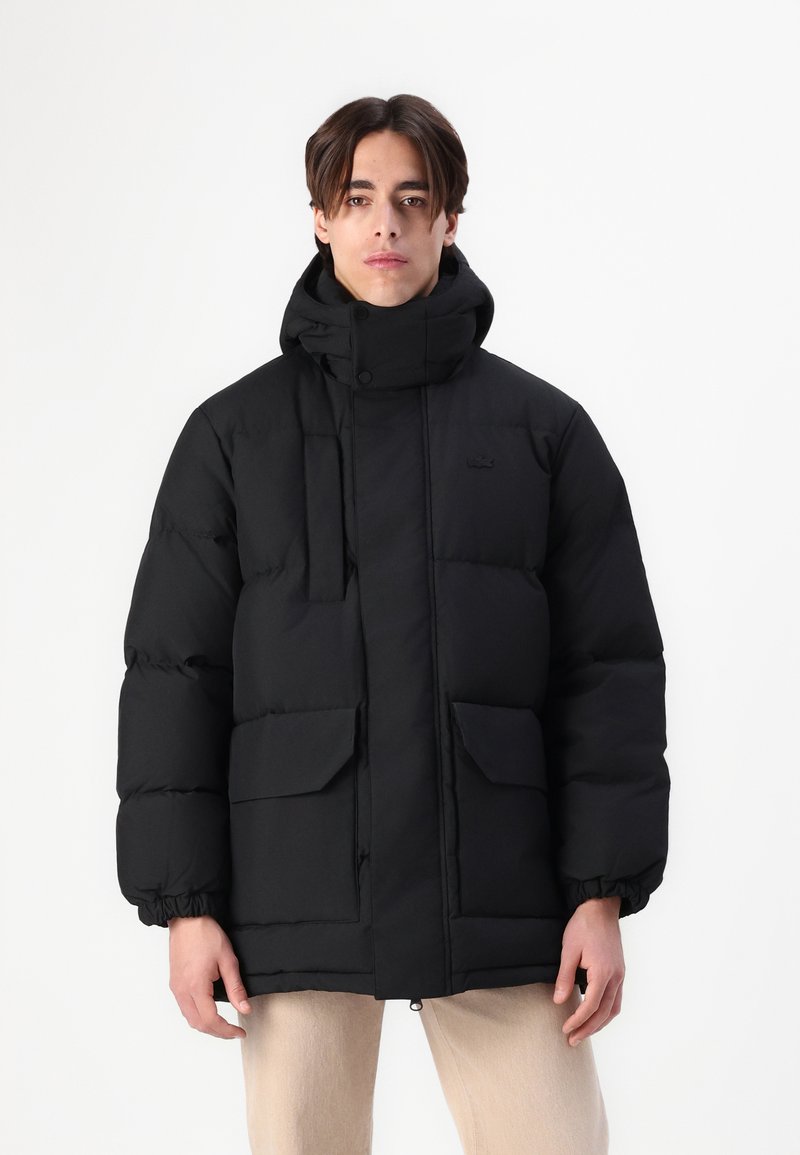Veste doudoune noire avec col haut, fermeture éclair à l'avant et fermetures pression. Comprend des poignets élastiques et deux grandes poches avant.