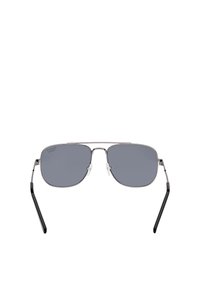 Lunettes de pilote avec une monture en métal argenté, des verres gris et des branches noires. Comprend des coussinets en silicone transparents et une forme de verres angulaire.