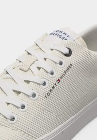 Baskets blanches Tommy Hilfiger en tissu texturé, lacets blancs, avec le logo représentant un drapeau rouge, blanc et bleu sur le côté et la languette.
