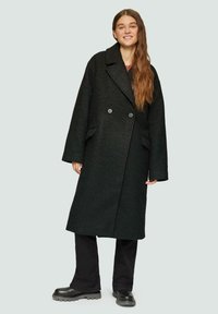 Zwarte wolblend jas met een dubbelgebreide ontwerp, grote revers, zijzakken en een oversized pasvorm. Gecombineerd met donkere broek en chunky laarzen.