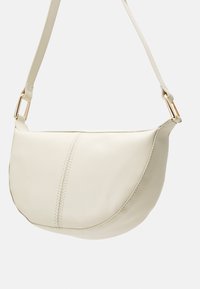 Borsa crossbody in pelle color crema con forma arrotondata, dettagli di cucitura sottili e accessori in metallo dorato sulla tracolla.