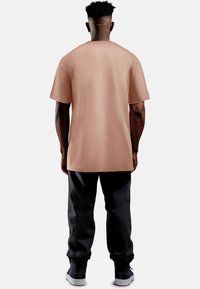 T-shirt marrone a maniche corte in cotone, vestibilità comoda, con scollo rotondo e orlo dritto, abbinata a pantaloni scuri e scarpe sportive.