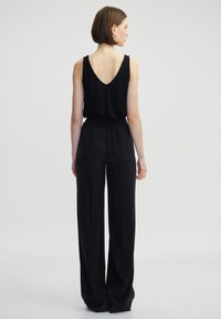 Černý top bez rukávů s V-zadním výstřihem, kombinovaný s volnými černými kalhotami s nařaseným pasem a měkkou texturou, zobrazený zezadu.