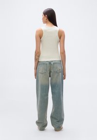 Ανοιχτό γκρι αμάνικη φανέλα, εφαρμοστή. Φοριέται με άνετα, ανοιζόγαλα τζιν που έχουν ξεβαμμένη υφή και πίσω τσέπες. Απλή, καθημερινή εμφάνιση.