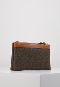 Brun lærredstaske med monogrammønster, lædertop og guldlynlås. Har en kompakt rektangulær form.