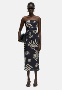 Trägerloses Kleid in Marineblau mit beigen botanischen Druckmotiven; figurbetont, knielanges Design; kombiniert mit schwarzen Accessoires und Sandalen.