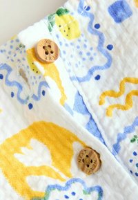 Tissu floral jaune et bleu avec deux boutons marron à quatre trous étiquetés "NEXT" cousus près des boutonnières.