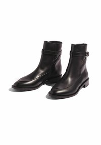 Botas de tobillo de piel negra con un diseño elegante, detalle de hebilla en el tobillo, punta afilada y un tacón bajo en bloque. Textura suave con acentos de costura.