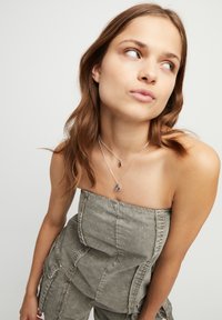 Collares en capas de plata con detalles de piedras preciosas moradas. La modelo lleva un top gris sin tirantes, mostrando la joyería de manera destacada.