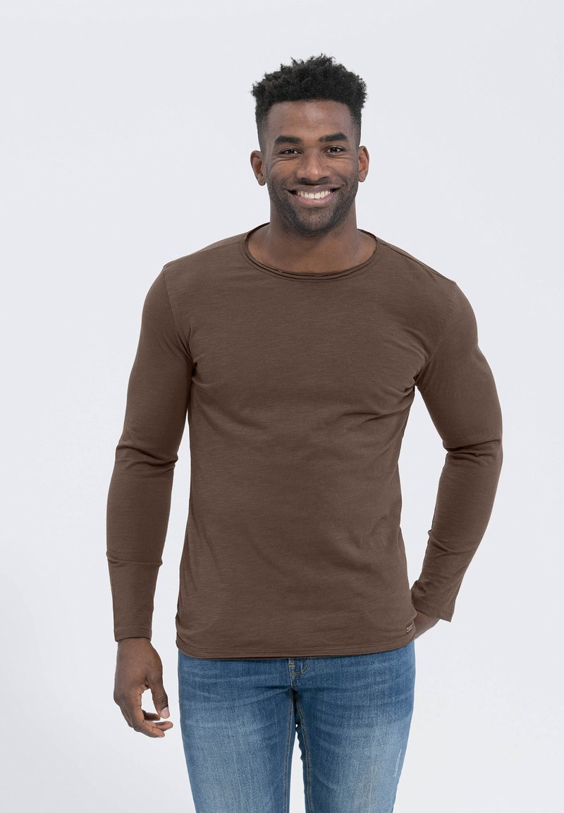 Braunes Langarmshirt aus weichem Stoff, mit Rundhalsausschnitt und figurbetontem Design, kombiniert mit blauen Jeans.