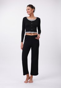Black cropped long-sleeve top with gray trim and buttons, paired with loose black pants. Smooth texture, comfortable fit, and relaxed design.