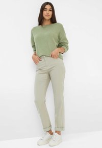 Pull en tricot vert clair, coupe décontractée, avec des manches longues. Pantalon gris clair, retroussé aux chevilles, associé à des baskets blanches. Design minimaliste.