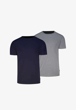 Mann trägt ein eng anliegendes dunkelblaues kurzärmeliges T-Shirt und hellgraue Boxershorts und steht mit entspannten Armen.