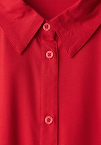 Camicia rossa con colletto, dal tessuto liscio, caratterizzata da bottoni rosa con il testo "Street Duo", che mette in risalto un design semplice e minimalista.