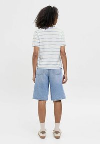 Camisa de manga corta a rayas azul claro y blanca combinada con pantalones cortos de mezclilla claros tipo Bermuda. Tela casual, corte relajado y bolsillos traseros visibles.