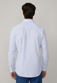 Lange mouwen shirt in lichtblauw met witte strepen. Heeft een klassieke kraag, knoopmanchetten en een gebogen zoom. Gemaakt van lichte stof.