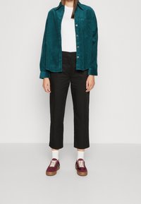 Koszula z zielonego sztruksu, biała koszulka, czarne spodnie o kroju cropped oraz bordowe tenisówki z białymi sznurowadłami i jasnobrązową podeszwą.