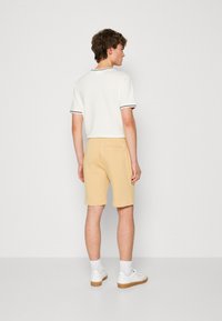 Biely polo s krátkym rukávom a tmavým prúžkovaným golierom, kombinovaný so svetlo béžovými šortkami. Model má na sebe biele tenisky so svetlými ponožkami.
