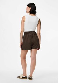 Pantalones cortos marrón con rayas, con una cinturilla elástica, combinados con una blusa blanca sin mangas. Presentando zapatos casuales con un patrón de vaca.