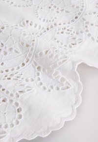 White fabric with intricate floral embroidery and scalloped edges featuring small cut-out details.
