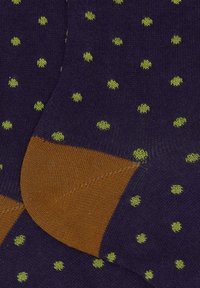 Marineblaue Socken mit kleinen grünen Pünktchen und kontrastierenden braunen Fersen und Zehen, die übereinander auf einer flachen Oberfläche liegen.