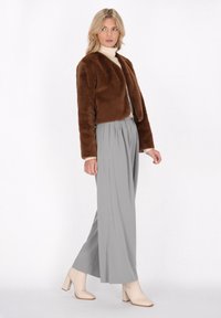 Bruine faux fur cropped jas, lange mouwen, drukknoopsluiting, gecombineerd met lichtgrijze geplooide broeken en beige enkellaarsjes, gladde textuur.