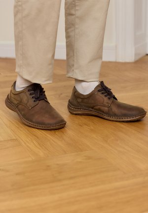 Braune Lederschuhe mit runden Zehen und strukturierten Oberflächen, ausgestattet mit dunklen Schnürsenkeln, sichtbaren Nähten und einer flachen Gummisohle.