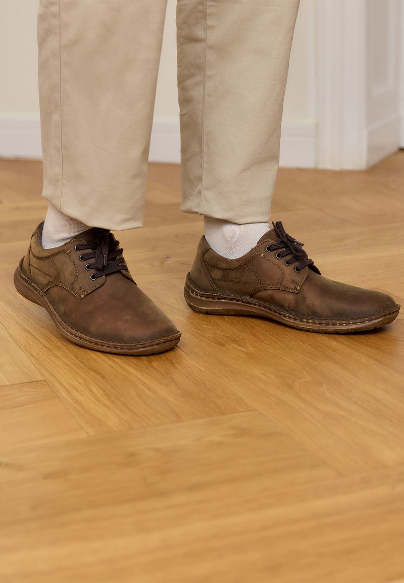 Braune Lederschuhe mit runden Zehen und strukturierten Oberflächen, ausgestattet mit dunklen Schnürsenkeln, sichtbaren Nähten und einer flachen Gummisohle.