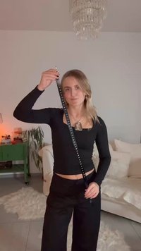 Μαύρη επιμηκυμένη ζώνη με ασημένιες καρφίτσες, κρατιέται κατακόρυφα, φορεμένη με εφαρμοστό μακρυμάνικο τοπ και φαρδιά παντελόνια σε φόντο με απαλό φωτισμό.