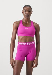 Fuksijas sporta krūšturis un šortu komplekts, izgatavots no elastīgas materiāla. Iekļauj nelielu baltu Nike logo krūšturī un "NIKE PRO" joslu šortos.