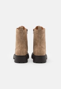 Bruna ankelstövlar i mocka med en slät textur, sidoförsedda med dragkedjor och svarta gummisulor. Brogue-detaljer längs överkanten.