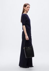 Μαύρη δερμάτινη τσάντα τύπου bucket με ομαλή υφή, στρογγυλεμένο σχήμα και κοντή λαβή. Η τσάντα διαθέτει στοιχεία από hardware σε χρυσό τόνο.