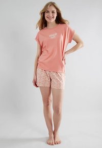 Light pink T-shirt with short sleeves featuring "GREAT DAY" text; paired with floral-patterned shorts in pastel colors. Soft, casual fabric.