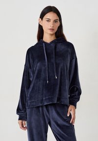 Granatowy welurowy hoodie o luźnym kroju, z długimi rękawami i kapturem ze sznurkiem. Posiada gładką fakturę i prążkowane akcenty na dole.